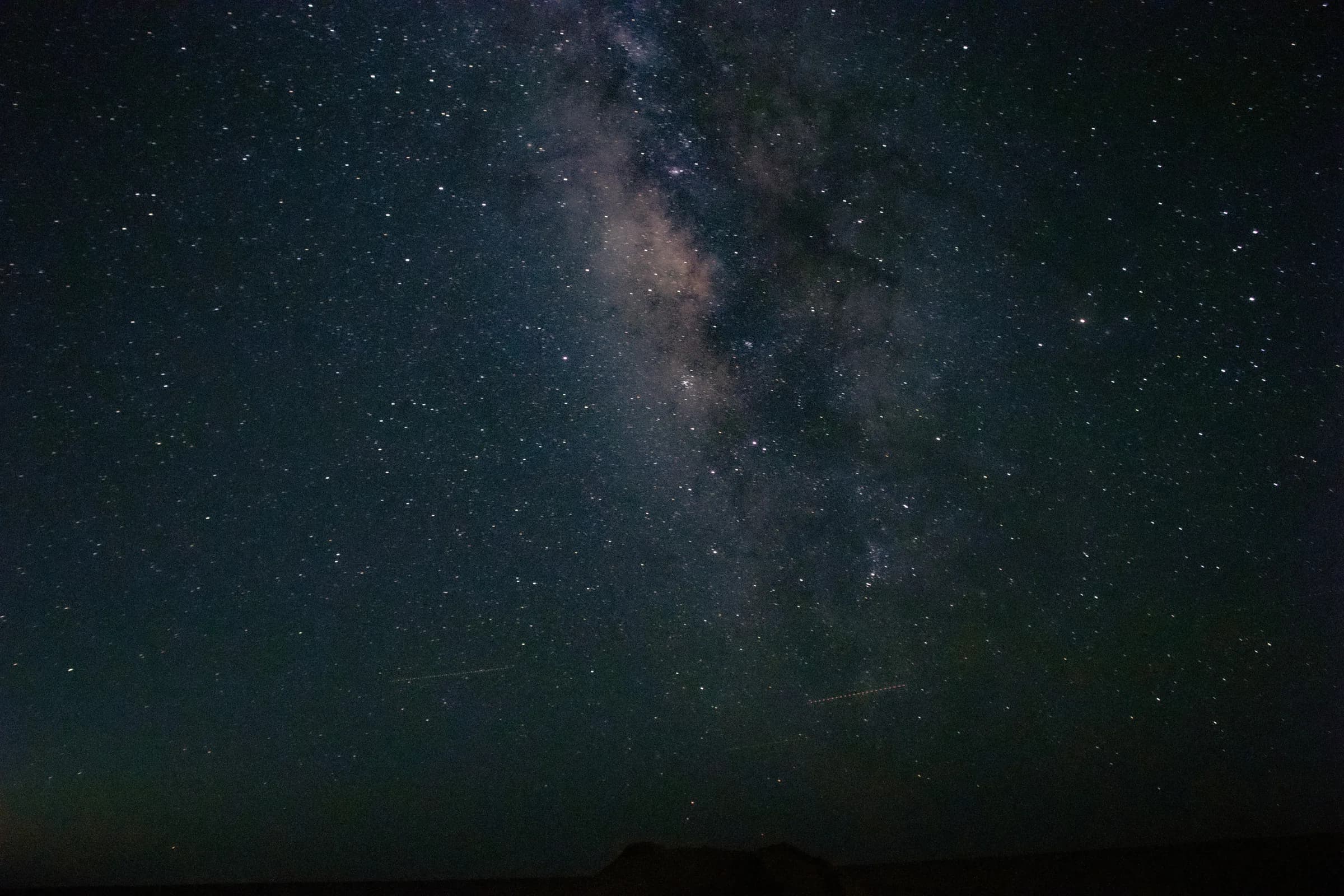 A wide-angle view of a dark night sky showcasing the distinct, luminous band of the Milky Way and numerous stars. Taken on a DSLR camera.